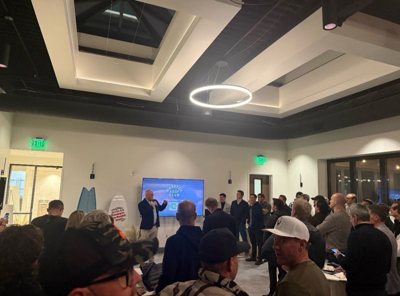 Launch event for The Wasatch Surf Club, with the club name on screen and a surfboard against the wall.