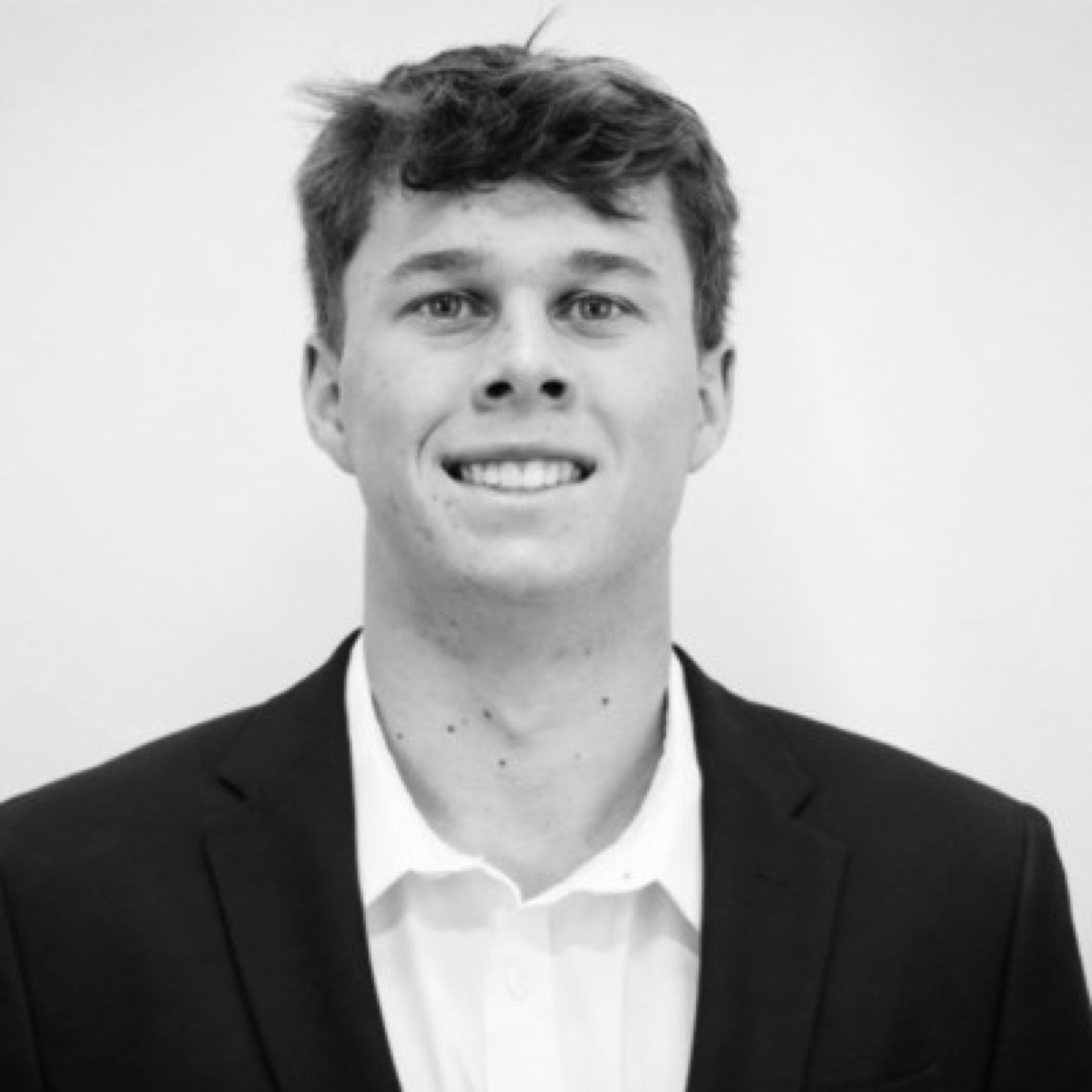 Black and white portrait of Zac Frailey, smiling, in a dark jacket and open collar.
